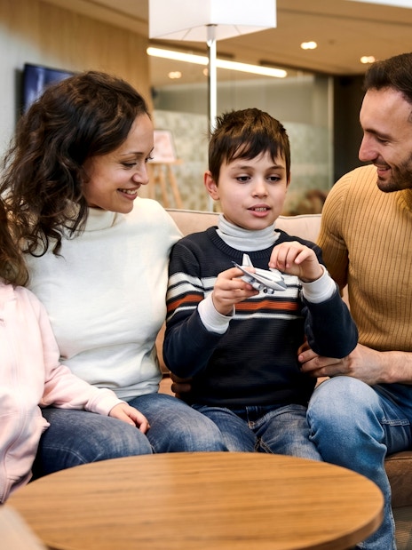 Family with children in airport VIP lounge holding toy airplanes.