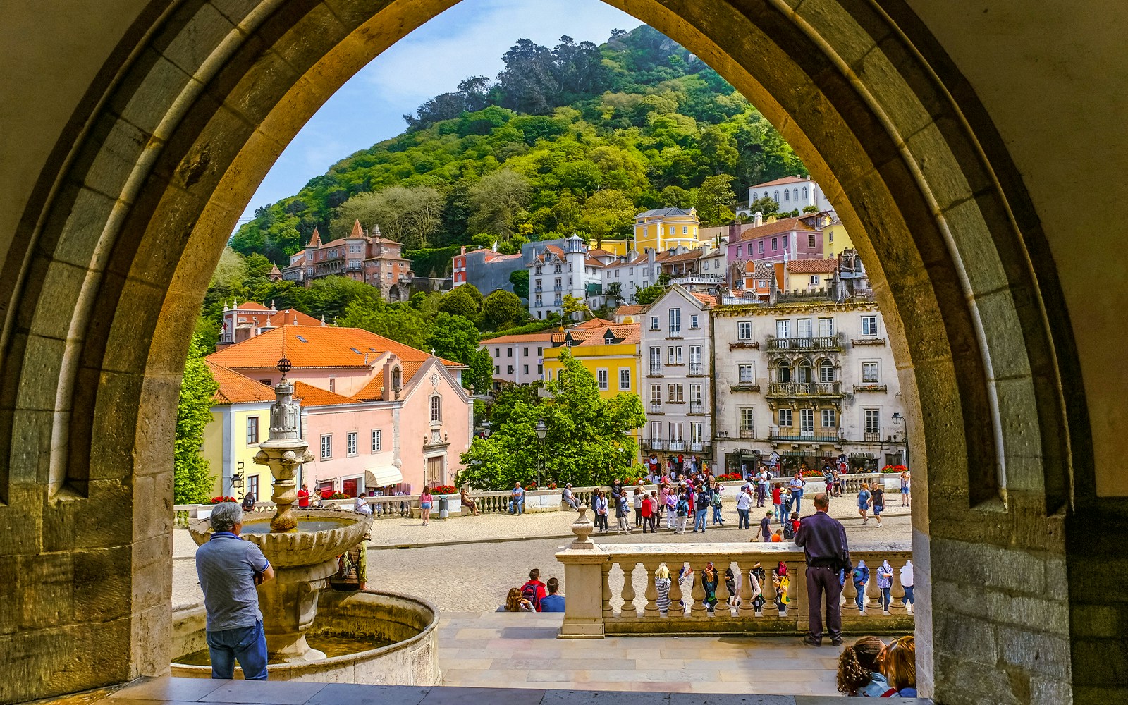 View of Sintra town square through an archway, featuring colorful buildings and a fountain.