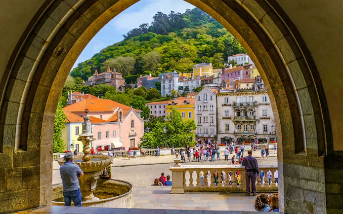 View of Sintra town square through an archway, featuring colorful buildings and a fountain.