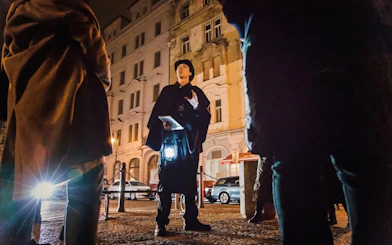 Tour guide with lantern leading Ghosts & Legends of Old Town Prague tour at night.