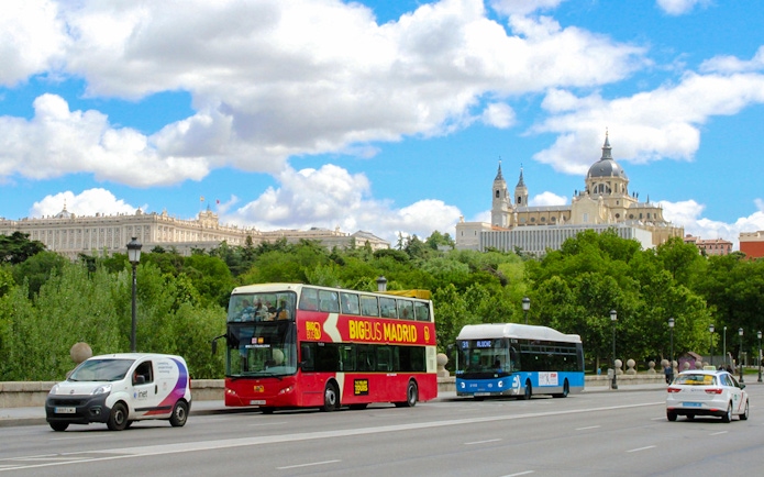 Big Bus touring Madrid street with Royal Palace and Almudena Cathedral in background.
