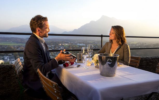 Couple dining with wine and panoramic view at Fortress Hohensalzburg, Salzburg.