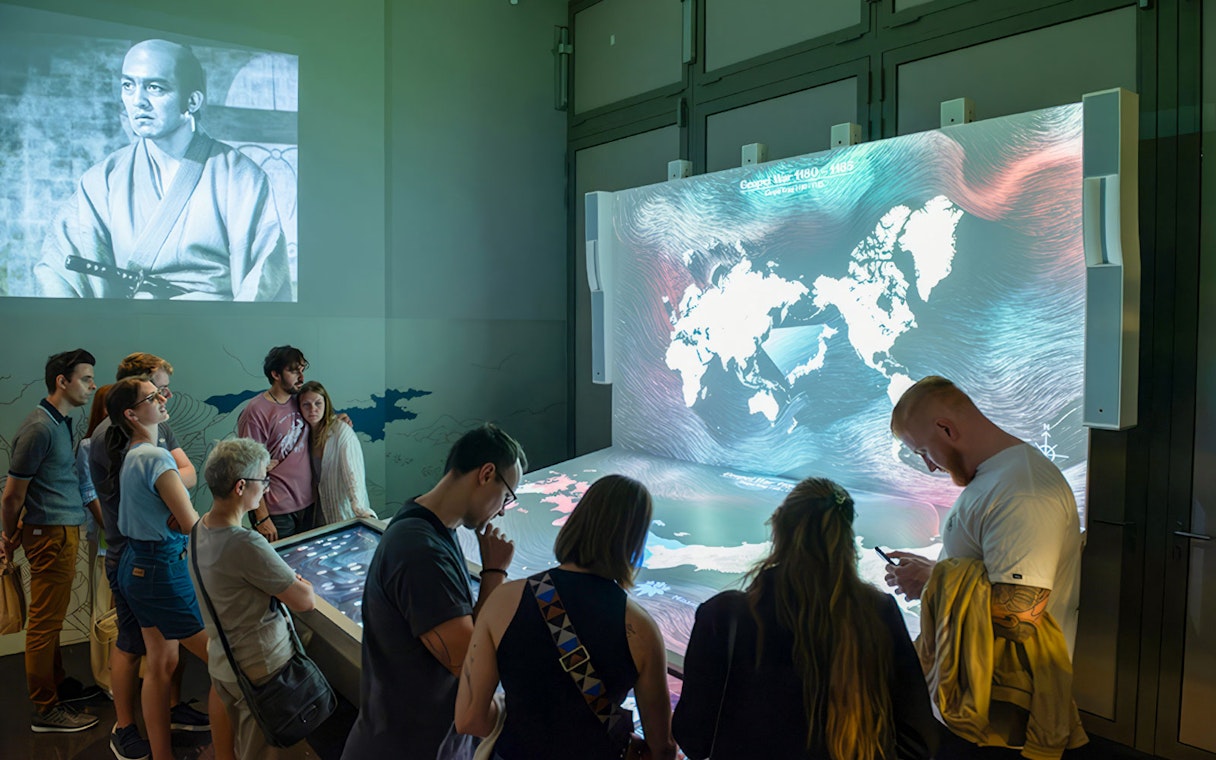 Visitors engaging with interactive display at Samurai Museum, featuring historical samurai imagery.