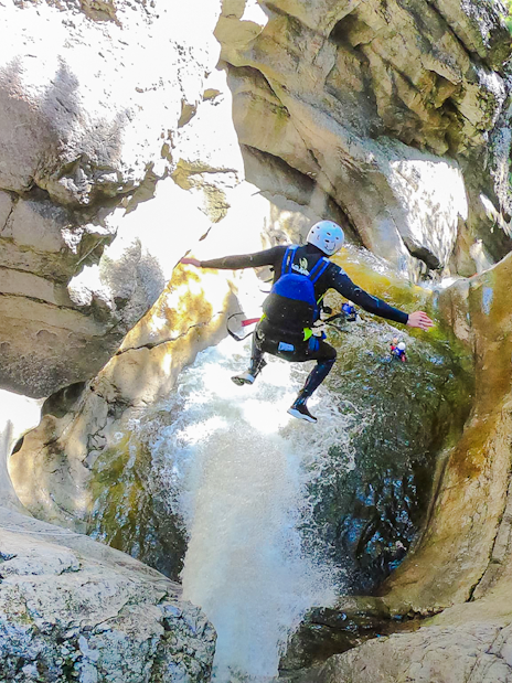 Person jumping into a canyon waterfall during a canyoning tour in Interlaken.