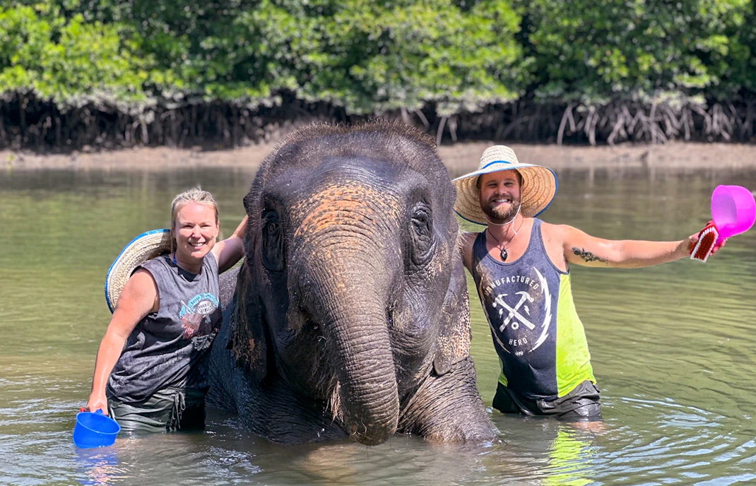 People bathing an elephant in a river at Krabi Elephant Shelter, Thailand.