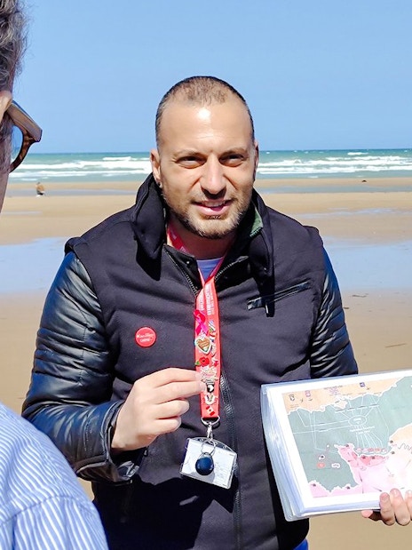 Tour guide explaining D-Day landing map on Normandy beach.