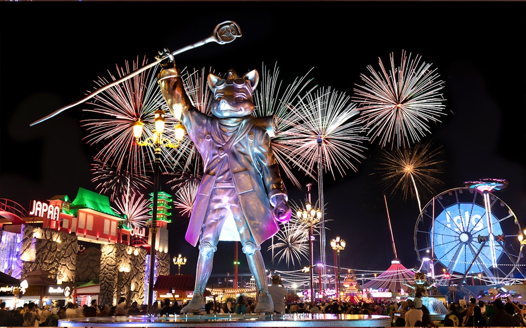 Fireworks over Global Village Dubai with large statue and Ferris wheel.