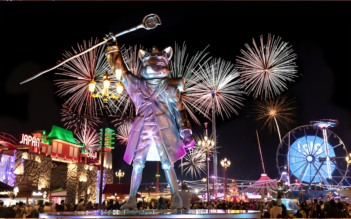 Fireworks over Global Village Dubai with large statue and Ferris wheel.