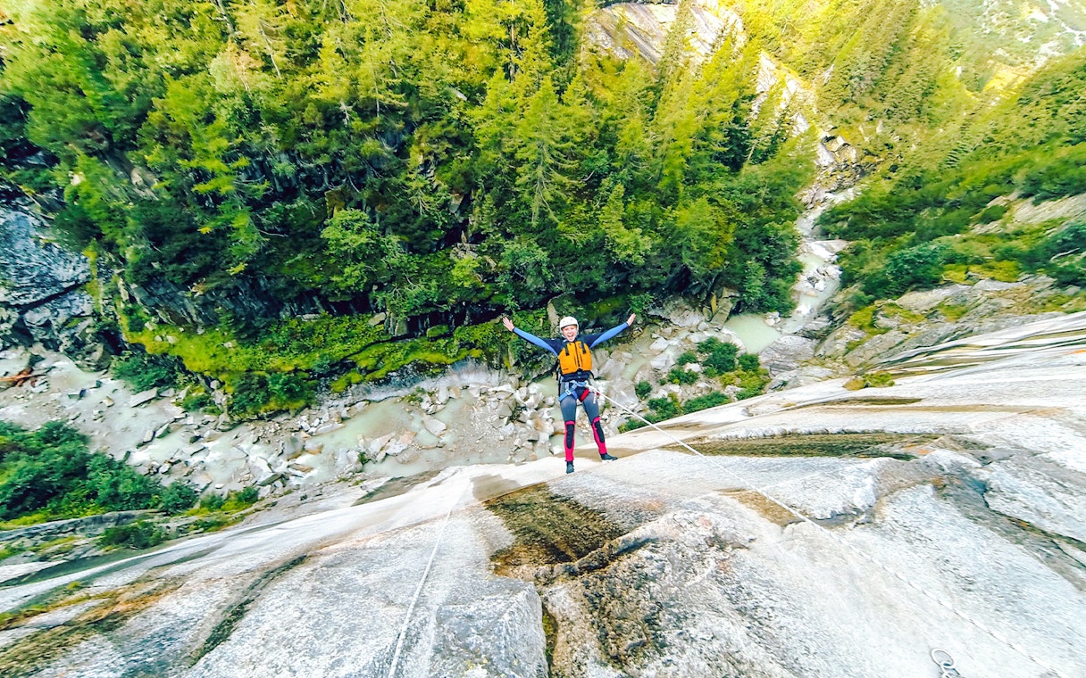 Person canyoning down a steep rock face in Interlaken, surrounded by lush forest.