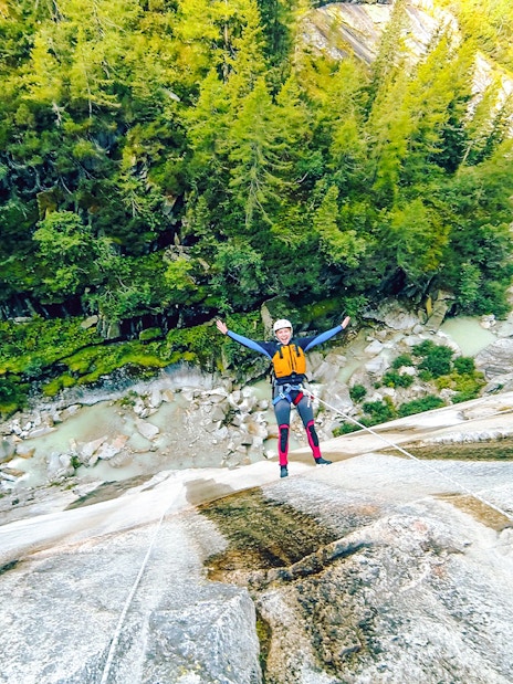 Person canyoning down a steep rock face in Interlaken, surrounded by lush forest.
