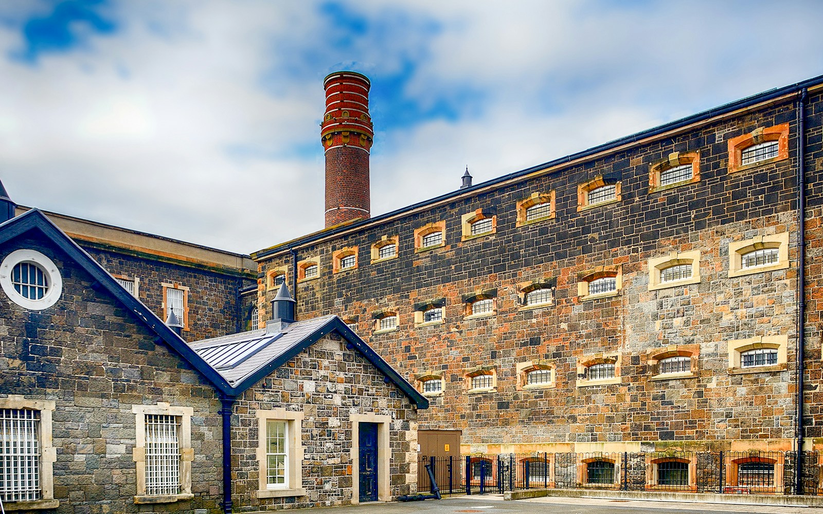 Historic stone prison building with barred windows and a tall chimney in Dublin, Ireland.