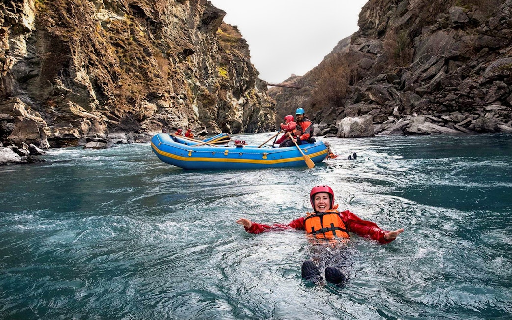 Tourist in life jacket swimming in Kawarau River during white water rafting adventure.