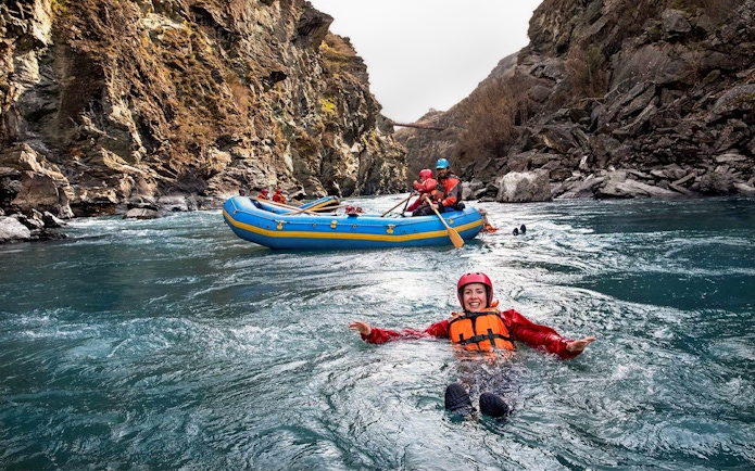 Tourist in life jacket swimming in Kawarau River during white water rafting adventure.