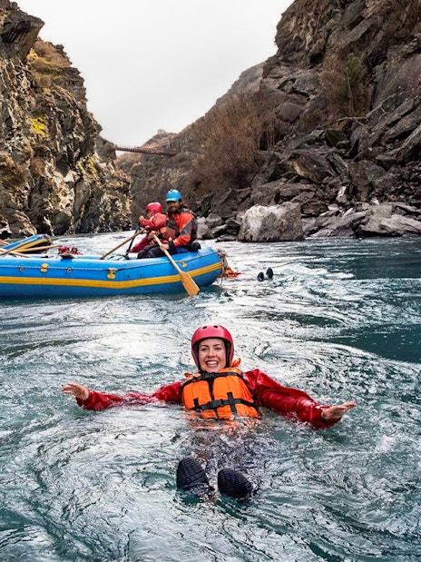 Tourist in life jacket swimming in Kawarau River during white water rafting adventure.