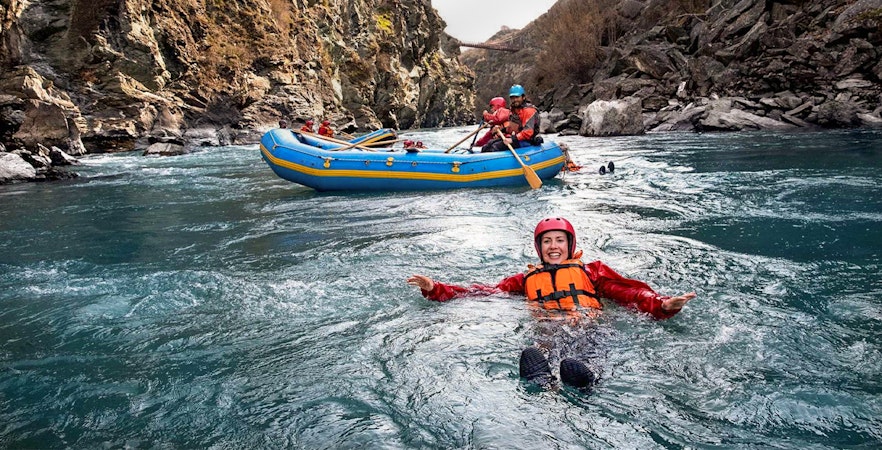 Tourist in life jacket swimming in Kawarau River during white water rafting adventure.