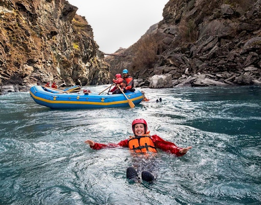 Tourist in life jacket swimming in Kawarau River during white water rafting adventure.