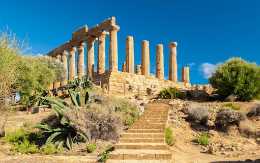 Ancient Greek temple ruins in Agrigento, Sicily, with stone columns and surrounding vegetation.