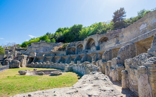 Ruins of the Archaeological Park of the Baths of Baiae, Naples, Italy, with ancient stone arches and greenery.