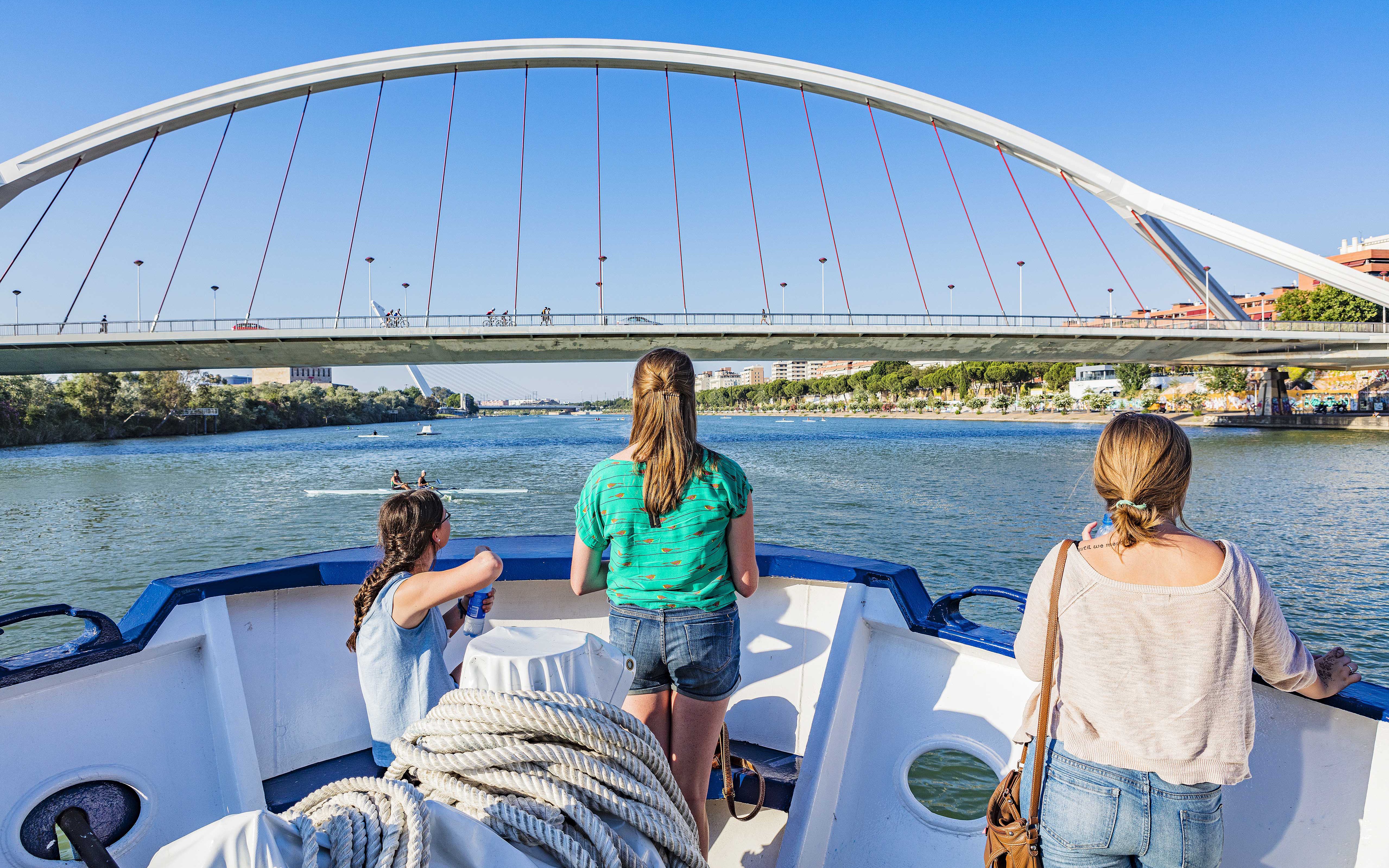 Tourists on a Seville Guadalquivir River cruise passing under a modern bridge.