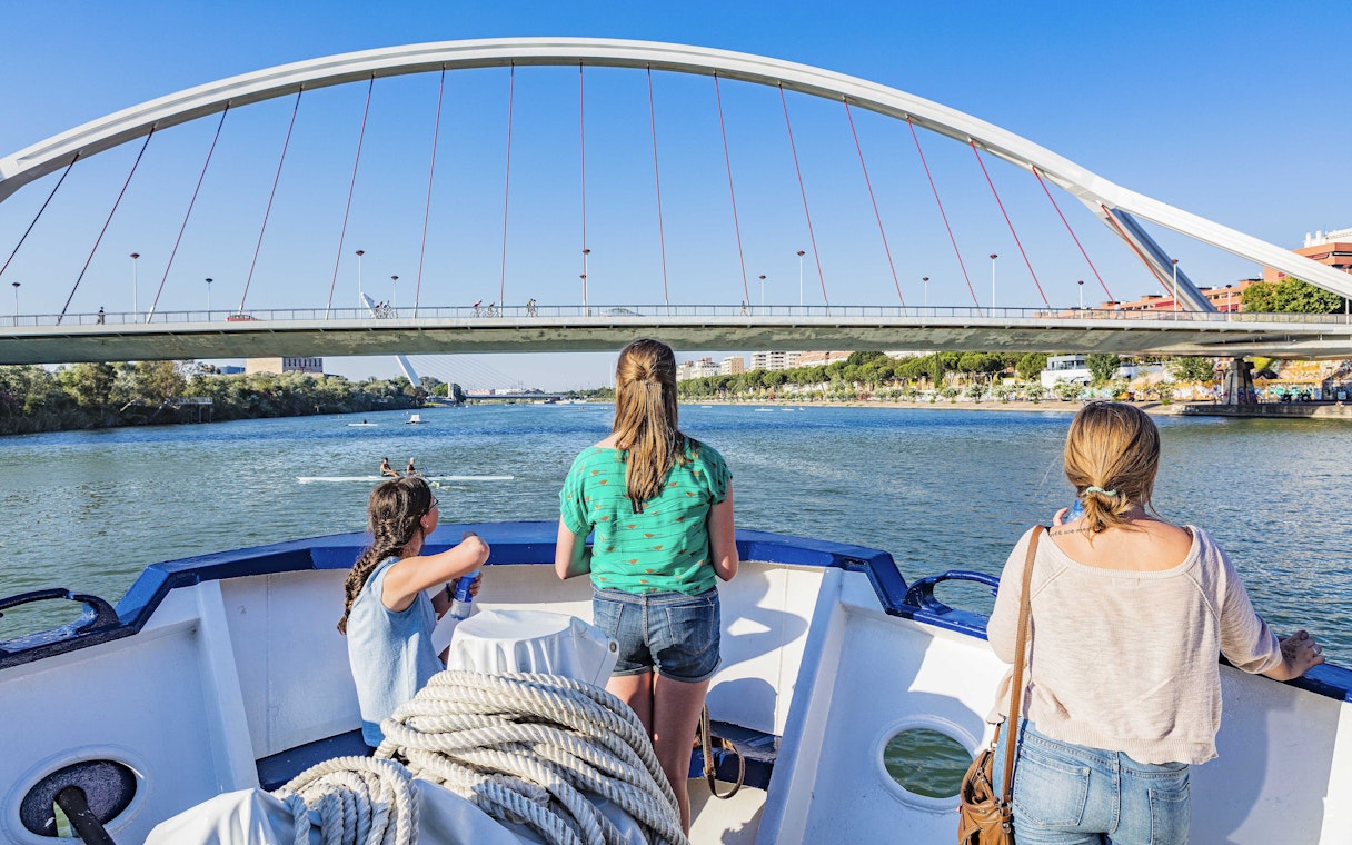 Tourists on a Seville Guadalquivir River cruise passing under a modern bridge.