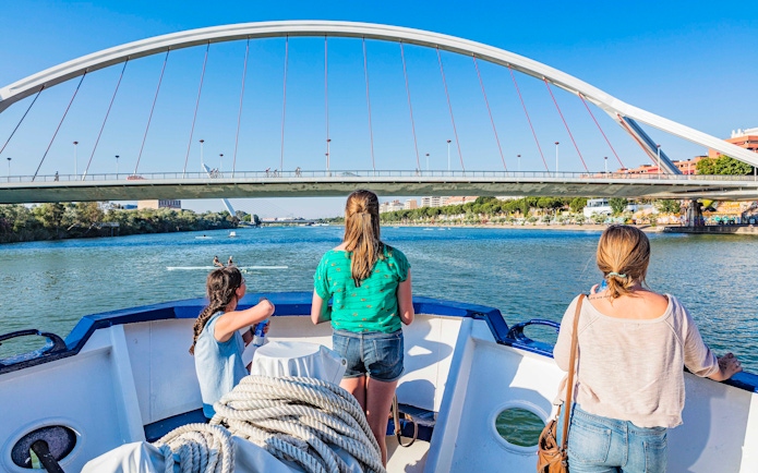 Tourists on a Seville Guadalquivir River cruise passing under a modern bridge.