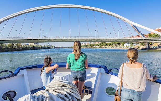 Tourists on a Seville Guadalquivir River cruise passing under a modern bridge.