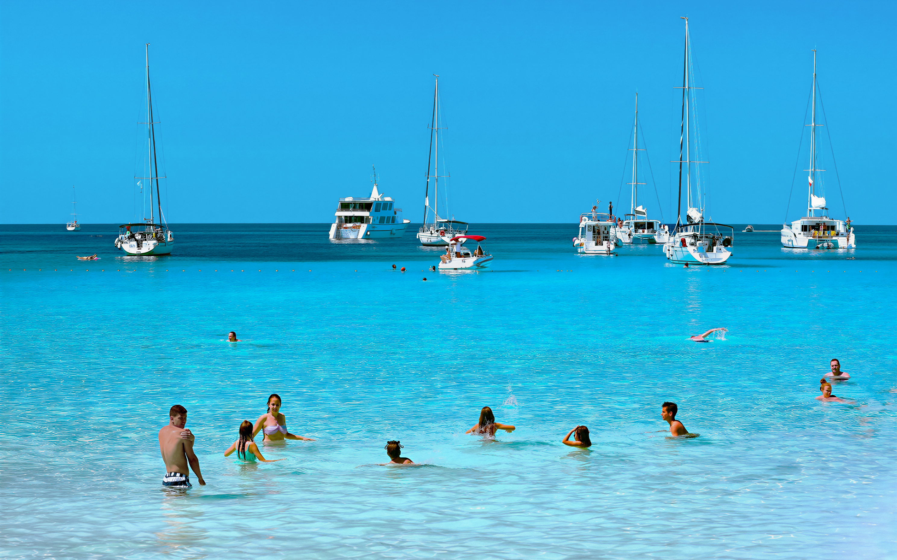 Guests swimming in clear waters with sailboats in Kornati National Park, Croatia.
