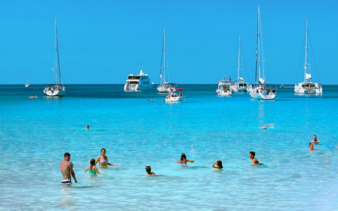 Guests swimming in clear waters with sailboats in Kornati National Park, Croatia.