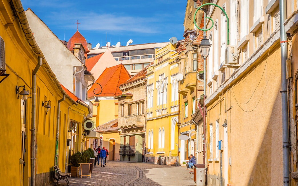 Street view of colorful historic buildings in Old Town, Brasov, with people walking.