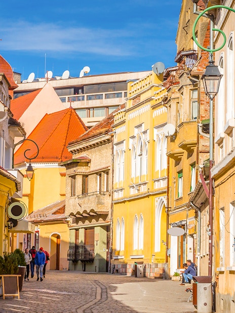 Street view of colorful historic buildings in Old Town, Brasov, with people walking.