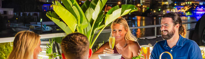 Dinner cruise guests enjoying drinks and food on the Gold Coast with city lights in the background.