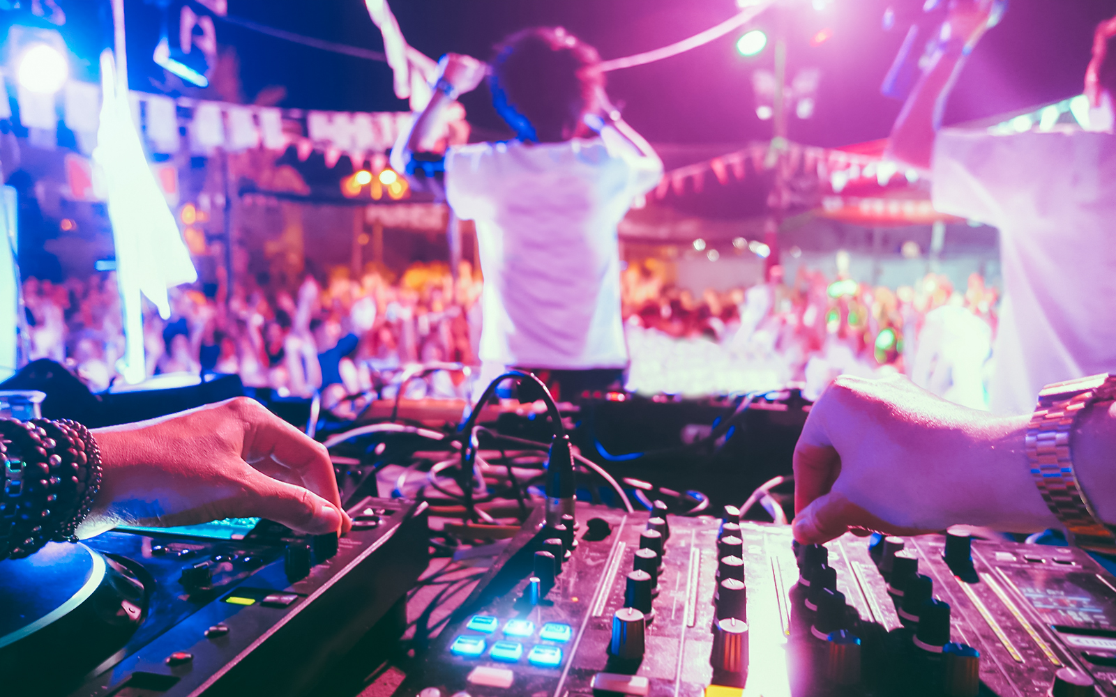 DJ mixing music at a vibrant beach party with a lively crowd in the background.