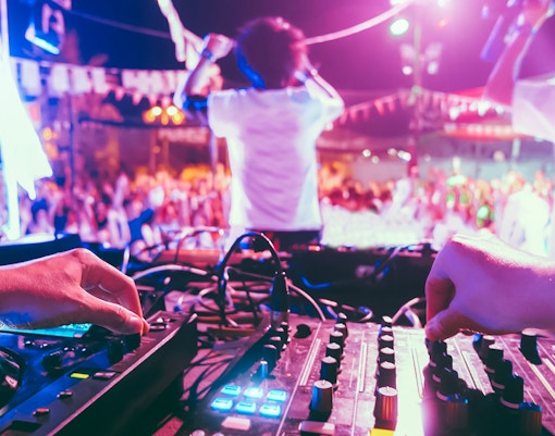 DJ mixing music at a vibrant beach party with a lively crowd in the background.