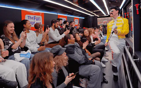 Tour group enjoying live performance on a bus with a performer in a yellow jacket.