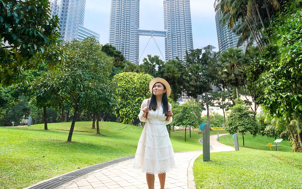 Person posing in park with Petronas Towers in Kuala Lumpur background.