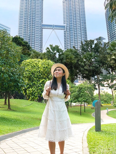 Person posing in park with Petronas Towers in Kuala Lumpur background.