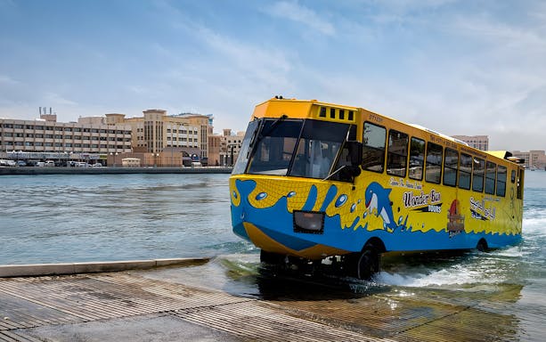 Dubai Wonder Bus entering water near city buildings.