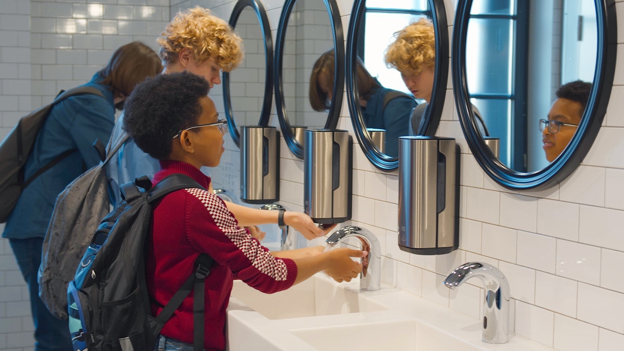 Kids washing hands at sinks in a public washroom.