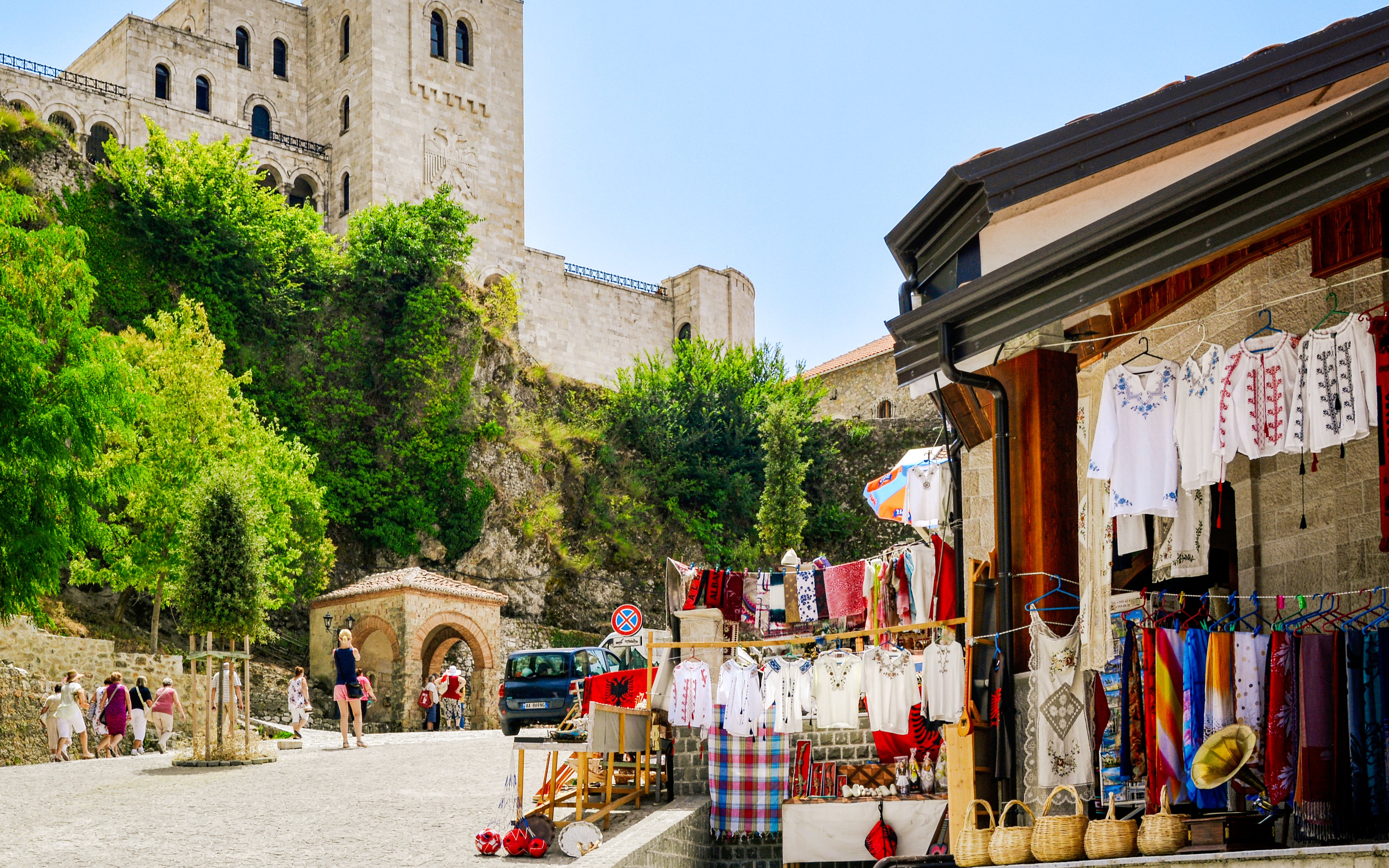 Market stalls with traditional clothing near Kruje Castle, Albania, with tourists exploring the area.