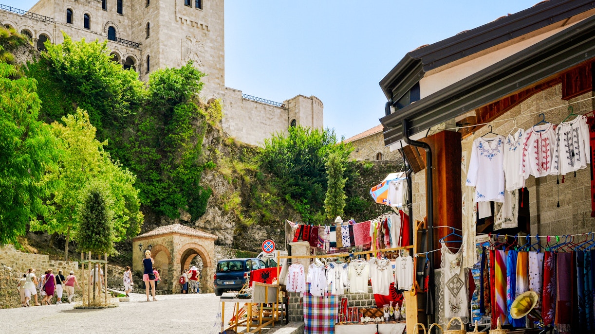 Market stalls with traditional clothing near Kruje Castle, Albania, with tourists exploring the area.