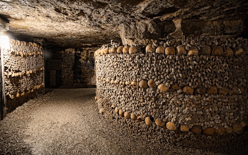 Bones stacked in the Paris Catacombs forming walls in a dimly lit tunnel.