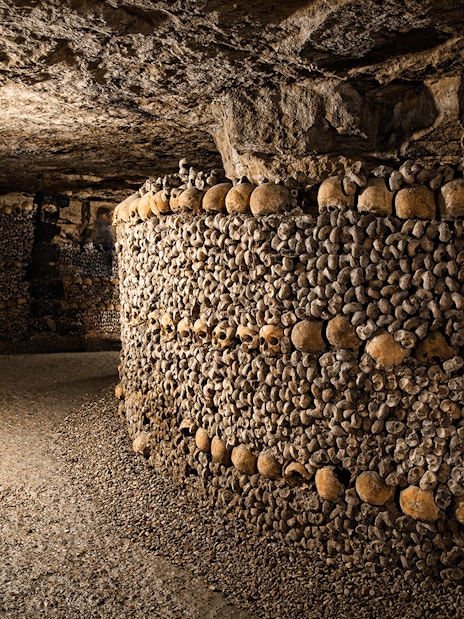 Bones stacked in the Paris Catacombs forming walls in a dimly lit tunnel.