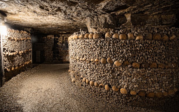 Bones stacked in the Paris Catacombs forming walls in a dimly lit tunnel.