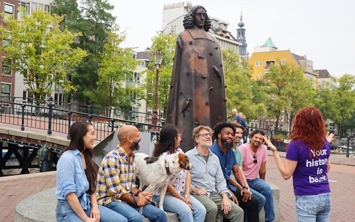 Group tour near a statue in Amsterdam with a guide explaining.