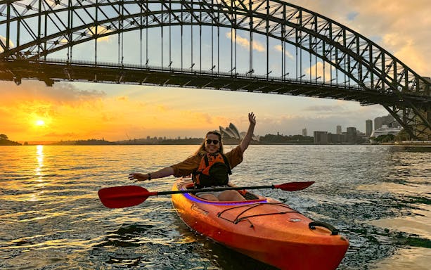 Kayaker on Sydney Harbour at sunrise near Harbour Bridge and Opera House.