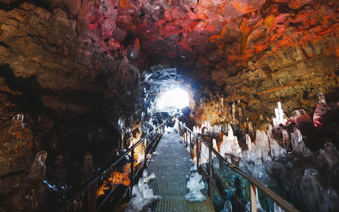 Walkway through Raufarhólshellir Lava Tunnel with ice formations and illuminated rock walls.