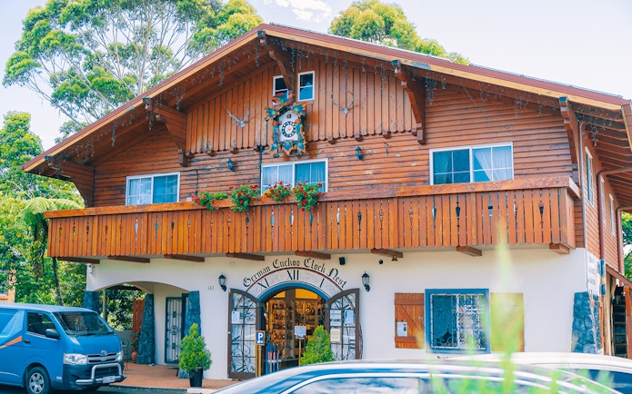 German Cuckoo Clock Nest on Tamborine Mountain, showcasing wooden architecture and vibrant flowers.
