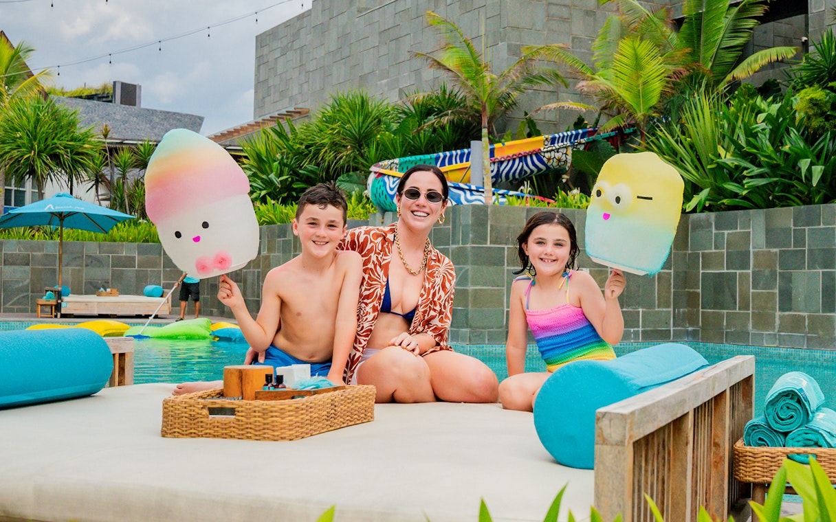Family enjoying daybeds at Atlas Beach Club, Bali, with colorful pool floats.