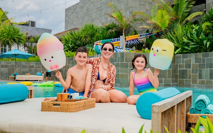 Family enjoying daybeds at Atlas Beach Club, Bali, with colorful pool floats.