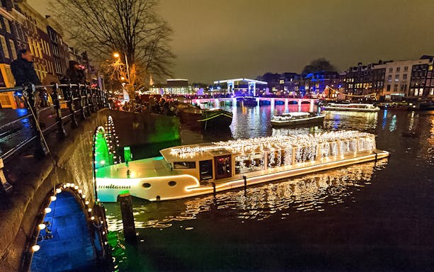 Amsterdam canal with illuminated boat during Light Festival cruise.